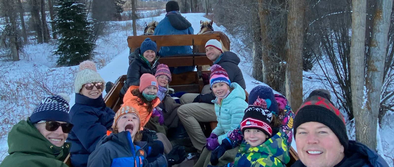 A Family Poses For A Group Photo While Enjoying A Vintage Wooden Sleigh Ride Through A Cottonwood Forest In Jackson Hole With Jackson Hole Vintage Adventures